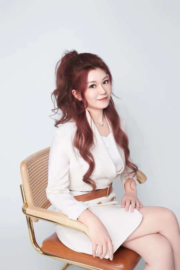 Portrait of Stella Zhou in a white suit, seated on a cane chair